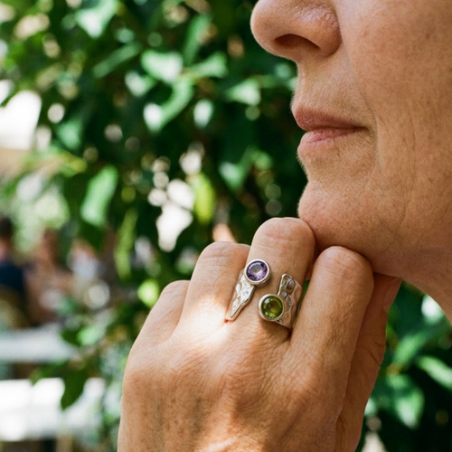 Silver dual stone hammered wide band ring worn outdoors, green and purple stones catching natural light, lush garden background
