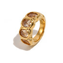 Gold hammered oval stone cocktail ring on white background, angled view showing four bezel-set champagne oval stones and rippled wide band detail
