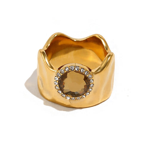 Wavy wide band crystal circle ring in gold, amber round stone with pavé surround on sculptural band, white background
