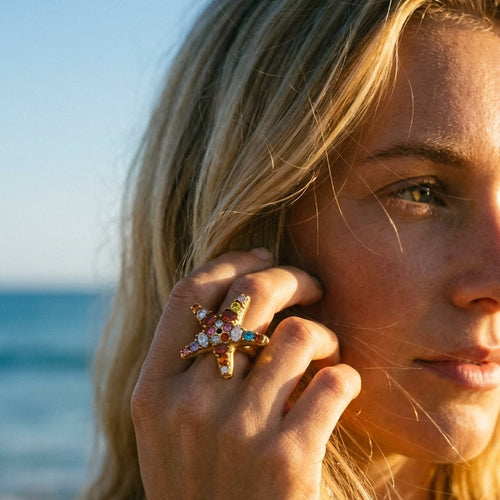 Woman wearing gold colorful crystal starfish ring at beach sunset, multicolor stones catching warm light
