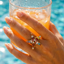 Gold crystal starfish ring worn poolside, multicolor stones in sunlight, hand holding iced drink
