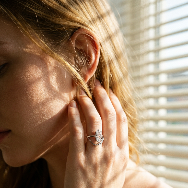 Woman wearing silver marquise crystal double band ring near window, warm morning light through blinds, hand touching hair
