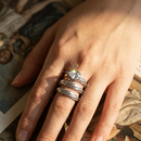 Silver spiral wrap ring worn on index finger resting on vintage magazine, crystal refracting light, moody indoor setting
