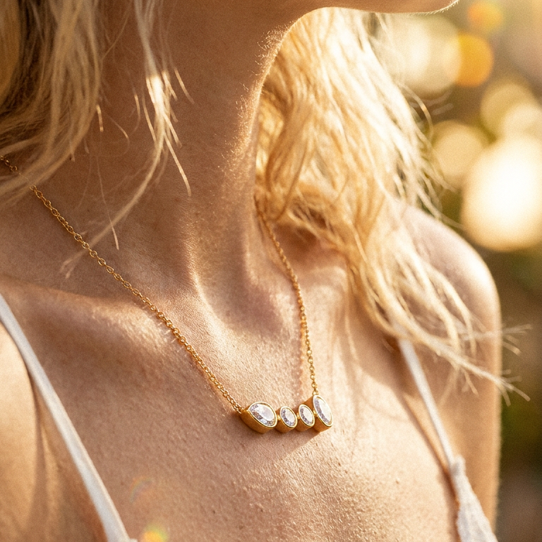 Close-up of gold graduated bezel stone bar necklace resting at collarbone, four bezel-set clear stones catching warm golden light, white strap visible, bokeh outdoor background
