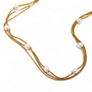 Gold layered pearl snake chain necklace flat lay, three parallel strands with round pearl stations, neutral background
