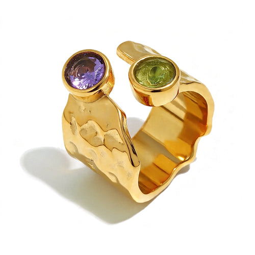 Gold hammered wide band ring close-up, bezel-set purple and green stones on open cuff band, white background

