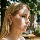 Woman wearing crystal flower stud earrings in gold outdoors, marquise CZ petal studs on ear, natural light
