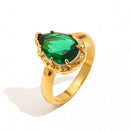 Gold green teardrop stone halo cocktail ring on white background, deep green faceted teardrop stone in multi-prong gold halo setting, tapered gold band, soft shadow
