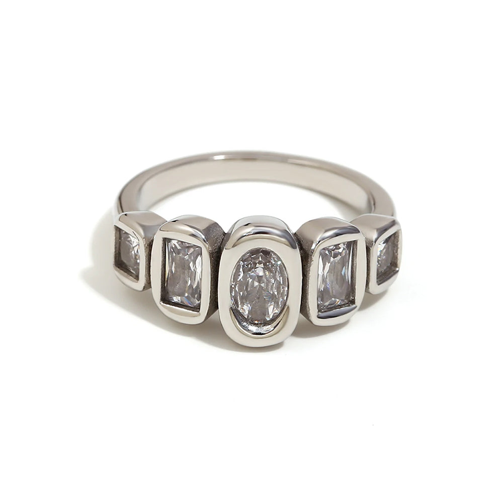 Silver oval and cushion multi-stone ring on white background, bezel-set oval center stone flanked by four cushion-cut accent stones, fine band shown in three-quarter angle, cool light with long shadow
