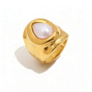 Gold hammered pearl chunky ring on white background, wide organic-surface band with bezel-set teardrop pearl at center, sculptural molten gold texture visible on band sides, long warm shadow
