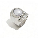 Silver hammered pearl chunky ring on white background, wide organic-surface band with bezel-set teardrop pearl at center, sculptural molten silver texture visible on band sides, long cool shadow
