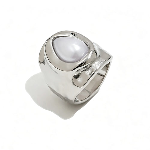 Silver hammered pearl chunky ring on white background, wide organic-surface band with bezel-set teardrop pearl at center, sculptural molten silver texture visible on band sides, long cool shadow
