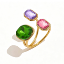 Gold triple stone open cocktail ring in Orchid colorway on white background, large emerald green cushion stone with lavender and rose octagon stones in graduated bezel settings, open band with warm shadow
