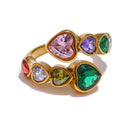 Gold multicolor heart stone open ring on white background, colorful heart-cut stones in alternating double-row arrangement showing pink, purple, green, red and olive stones in gold bezel settings, open adjustable band
