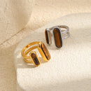 Gold and silver dual tiger's eye rings on textured cream stone surface, open band structure and stone grain visible
