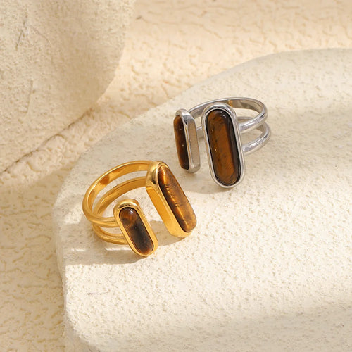 Gold and silver dual tiger's eye rings on textured cream stone surface, open band structure and stone grain visible
