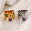 Gold and silver dual stone hammered rings front view on cream fabric, bezel-set green and purple stones, open band detail
