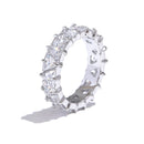Silver heart-cut eternity ring standing upright on white background, full band of heart-shaped stones in four-prong settings, cool light highlighting stone facets and prong detail, long cool shadow beneath
