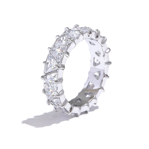 Silver heart-cut eternity ring standing upright on white background, full band of heart-shaped stones in four-prong settings, cool light highlighting stone facets and prong detail, long cool shadow beneath
