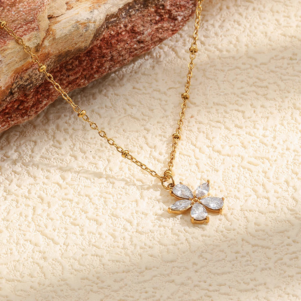 Gold crystal flower pendant necklace flat lay on textured cream surface, warm tone styling
