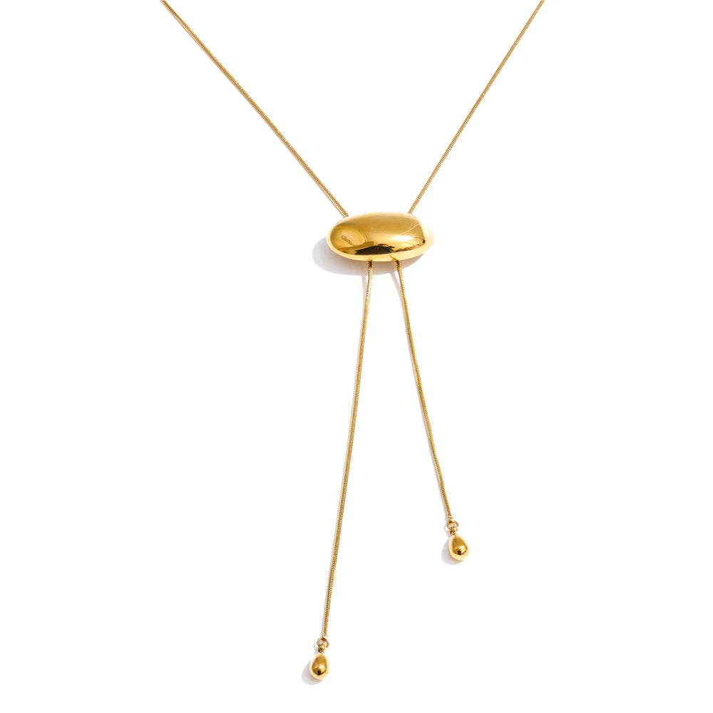 Gold oval slider lariat necklace on white background, polished dome oval sliding along fine snake chain, two ends hanging at uneven lengths with teardrop tips, soft shadow beneath oval slider
