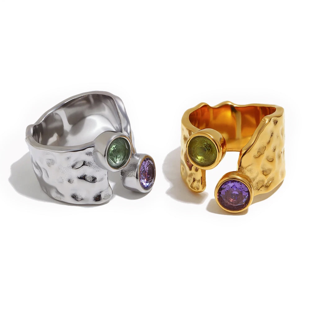 Dual stone hammered wide band ring in gold and silver, bezel-set green and purple stones, open back construction, white background
