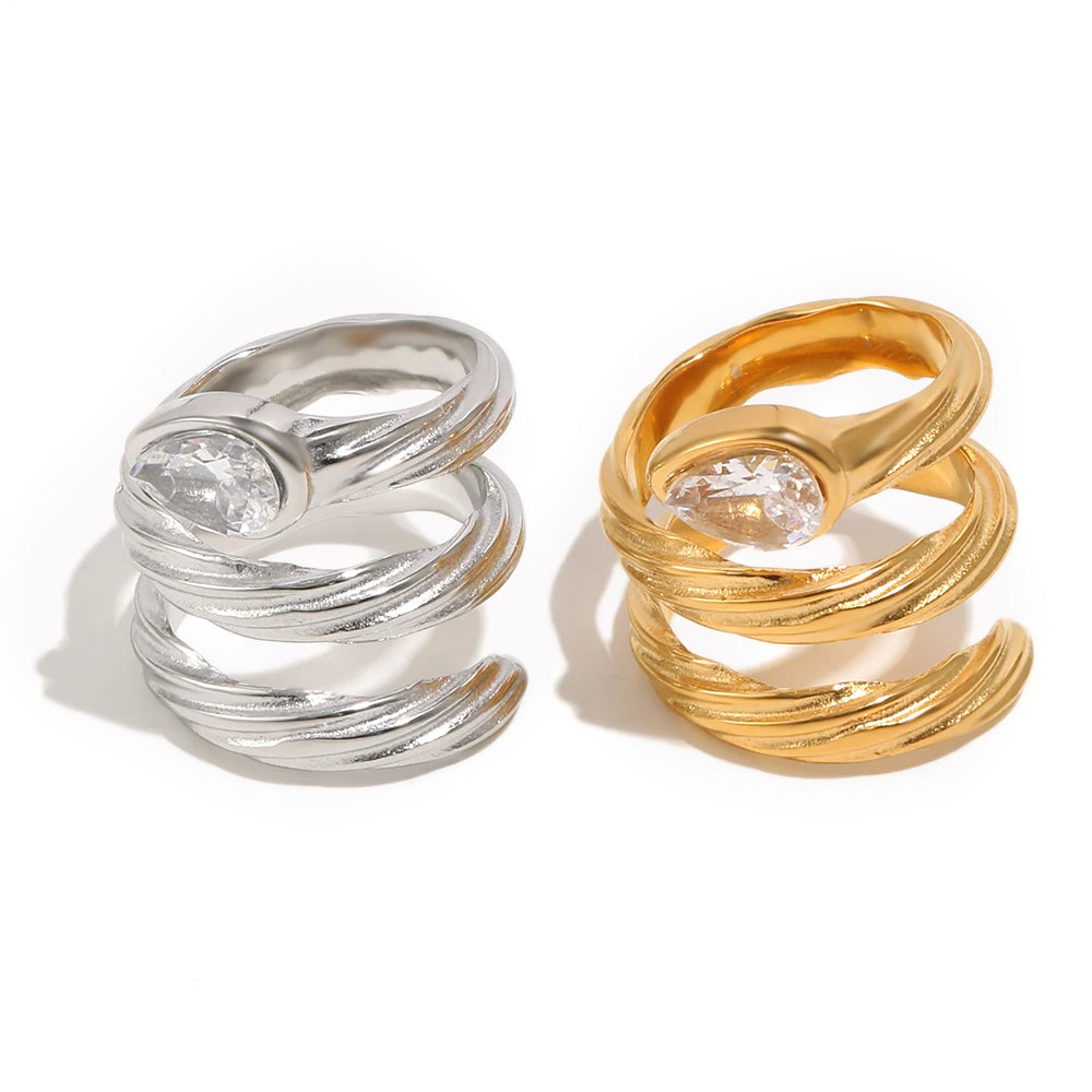 Spiral wrap ring in gold and silver, bezel-set pear-cut crystal at crown, textured coiling band, white background

