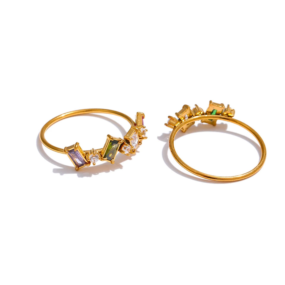 Two gold geometric multi-stone rings on white background, multicolor ring shown front-facing with purple, olive and clear baguette stones, tonal ring shown side angle revealing fine band profile and prong setting detail, warm light
