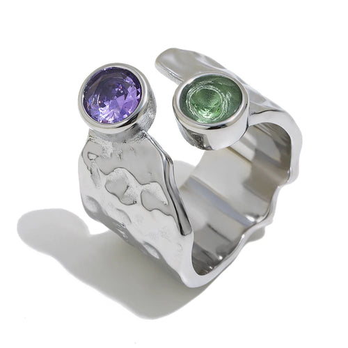 Silver hammered wide band ring close-up, bezel-set purple and green stones on open cuff band, white background
