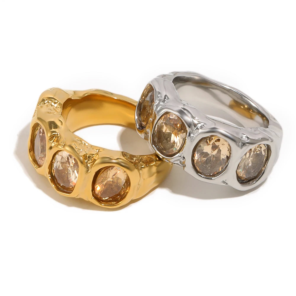 Gold and silver hammered oval stone cocktail rings stacked on white background, four bezel-set champagne oval stones on wide rippled band
