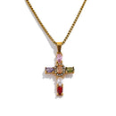 Gold multicolor stone cross pendant necklace on white background, full necklace view showing gold box chain and cross pendant with pink, orange, purple, olive, clear and red oval stones, warm directional light
