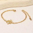 Gold pearl coin charm Figaro chain bracelet laid on cream stone surface, engraved coin charm with four pearl accents, alternating Figaro chain links, lobster clasp extender and branded tag visible, warm directional light
