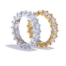 Gold and silver heart-cut eternity rings standing upright on white background, full band of heart-shaped stones in four-prong settings around both rings, warm and cool metal colorways shown side by side, long soft shadows
