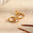 Two gold green stone pavé heart charm hoop earrings on white marble surface, one showing pavé hoop face and heart charm, one showing back, tortoiseshell hair clip nearby
