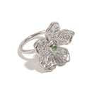Silver hammered texture flower ring on white background, angled view showing five sculptural petals, green stone center, and smooth rounded band
