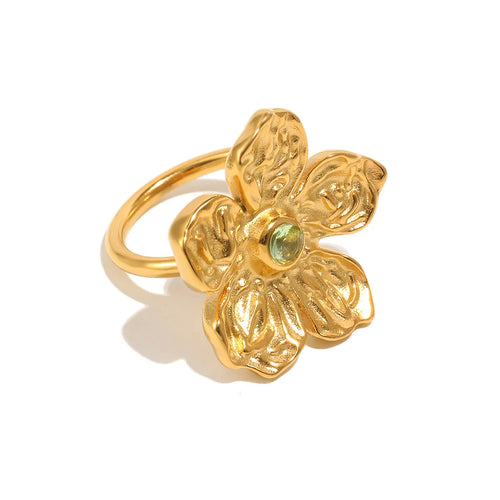 Gold hammered texture flower ring on white background, angled view showing five sculptural petals, green stone center, and smooth rounded band
