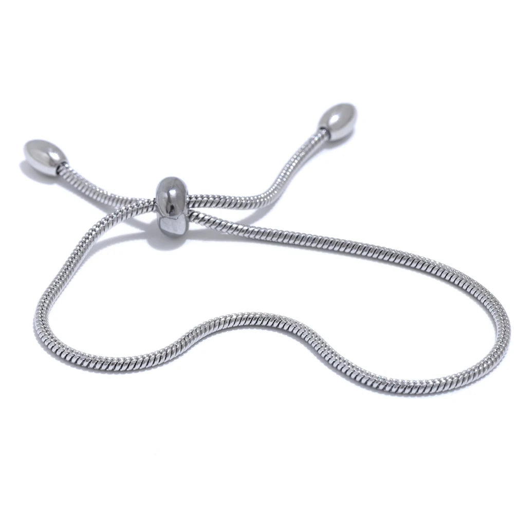 Silver snake chain slider bracelet on white background, S-curve layout showing barrel slider at center with two snake chain ends tipped with polished ovals, cool light with soft shadow
