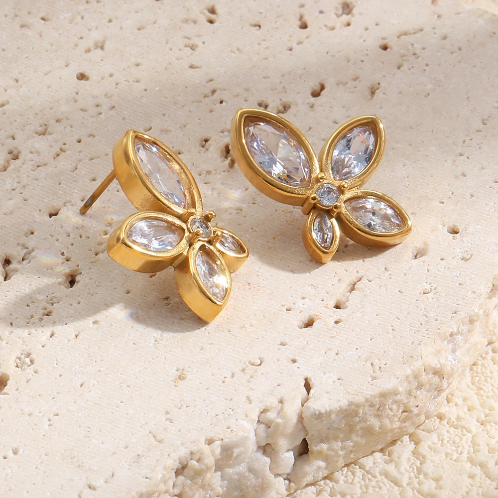 Gold crystal flower stud earrings flat lay on textured stone surface, four petal CZ design
