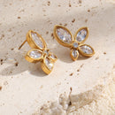 Gold crystal flower stud earrings flat lay on textured stone surface, four petal CZ design
