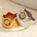Gold and silver wavy wide band rings on cream knit surface, interior band visible, amber crystal halo detail
