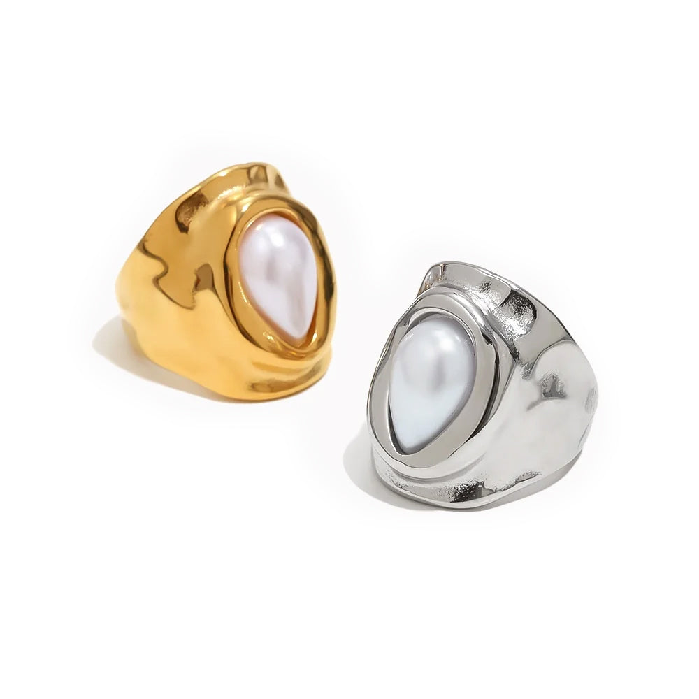 Gold and silver hammered pearl chunky rings on white background, both showing wide organic-surface band with bezel-set teardrop pearl at center, side by side comparison

