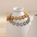 Gold and silver multicolor square stone tennis bracelets draped over white ceramic vase neck, both colorways showing pastel square stones in star-prong settings side by side, warm cream background
