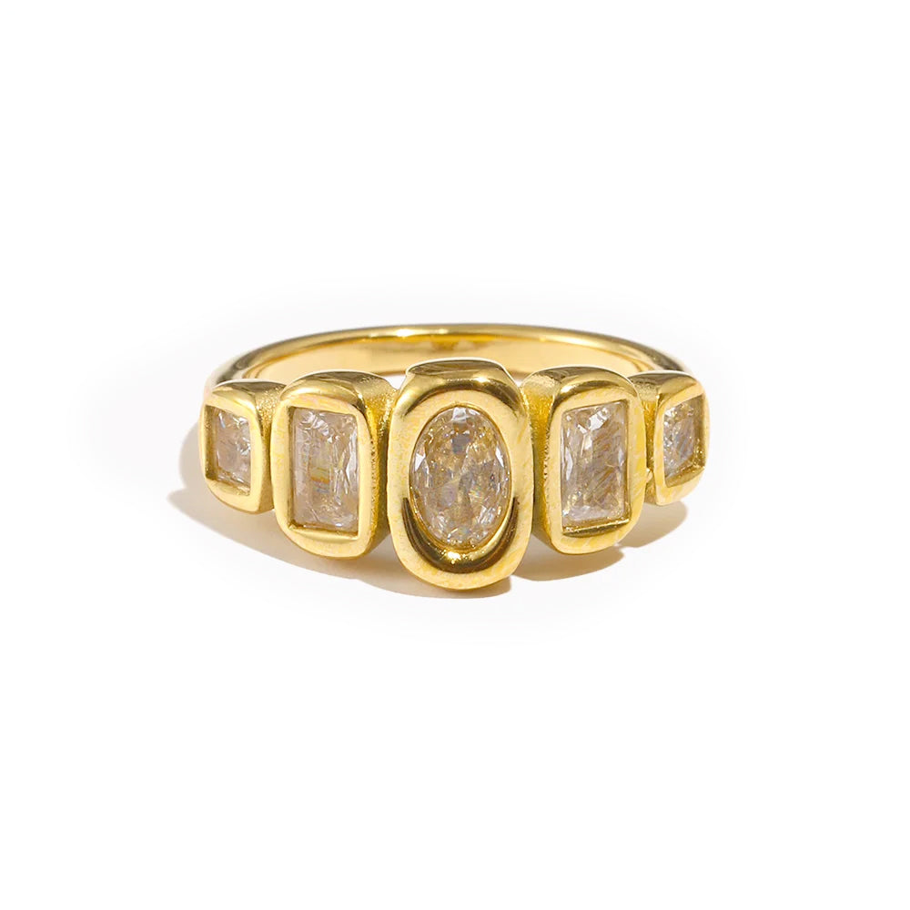 Gold oval and cushion multi-stone ring on white background, front-facing view showing five bezel-set stones across full ring width, oval center stone and four cushion accent stones in warm light
