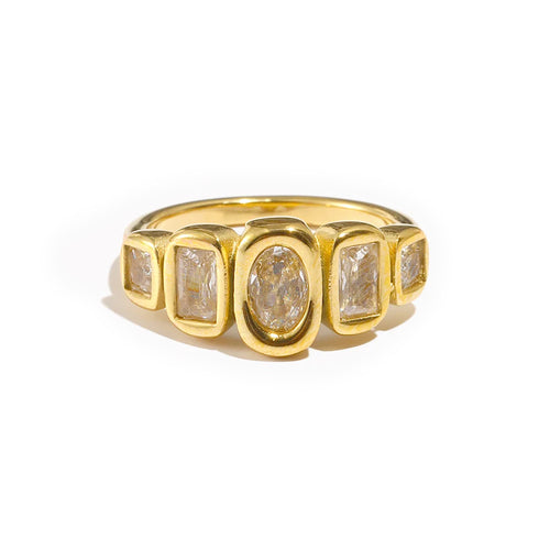 Gold oval and cushion multi-stone ring on white background, front-facing view showing five bezel-set stones across full ring width, oval center stone and four cushion accent stones in warm light
