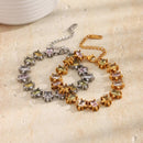 Gold and silver multicolor square stone tennis bracelets overlapping on cream textured stone surface, star-prong settings and pastel square stones of both colorways visible, lobster clasps and extender chains shown, warm angled light
