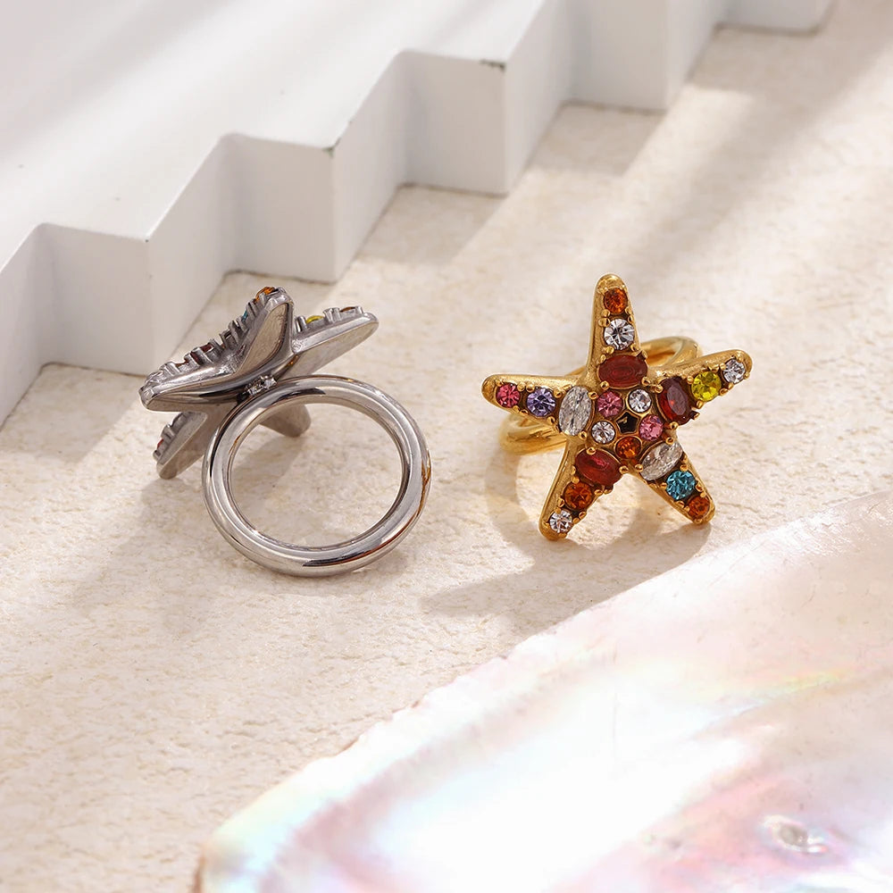 Gold and silver crystal starfish rings on textured stone surface, side view showing band and stone setting
