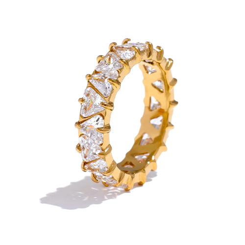 Gold heart-cut eternity ring standing upright on white background, full band of heart-shaped stones in four-prong settings, warm light showing stone facets and open prong structure, long warm shadow beneath
