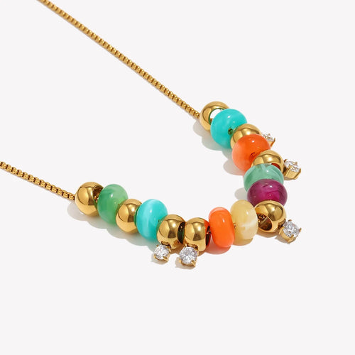 Close-up of gold colorful resin bead station necklace on white background, multicolor resin beads in turquoise coral amber and plum alternating with gold spheres, three clear stone stations visible, warm directional shadow
