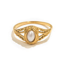 Gold filigree freshwater pearl ring on white background, oval cream pearl in beaded bezel surrounded by open scrollwork filigree frame, fine band tapering toward shank, soft warm shadow beneath

