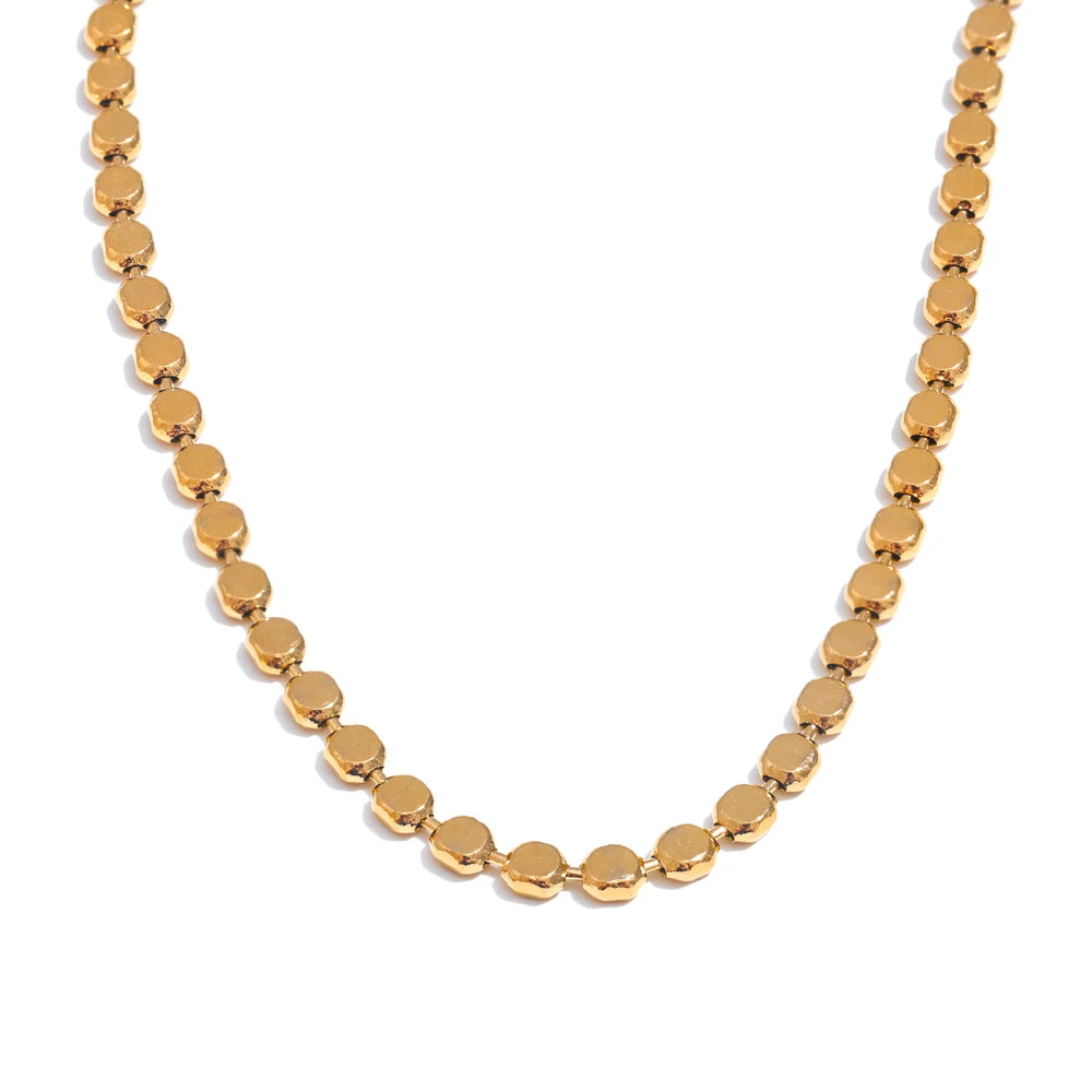 Gold disc chain necklace on white background, continuous flat disc links in U-shape, mirror-polished round discs with thin edges visible, warm white background with soft shadow beneath
